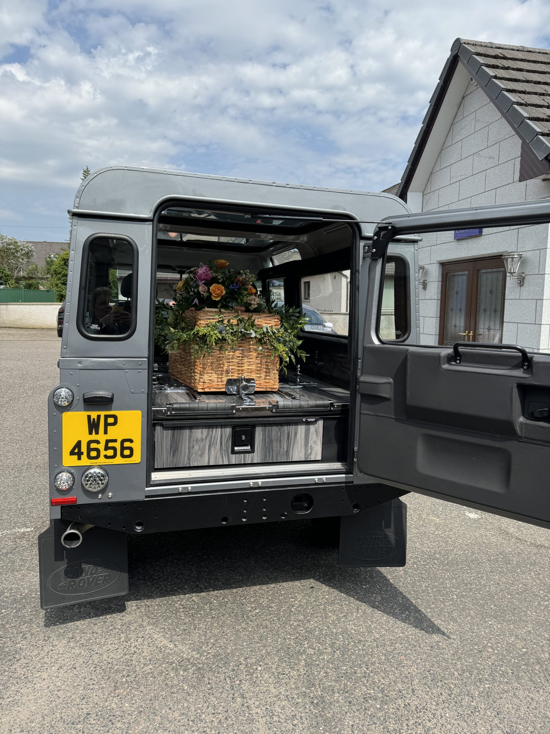 A Land Rover Defender Hearse with the back door open during a car enthusiast's funeral.