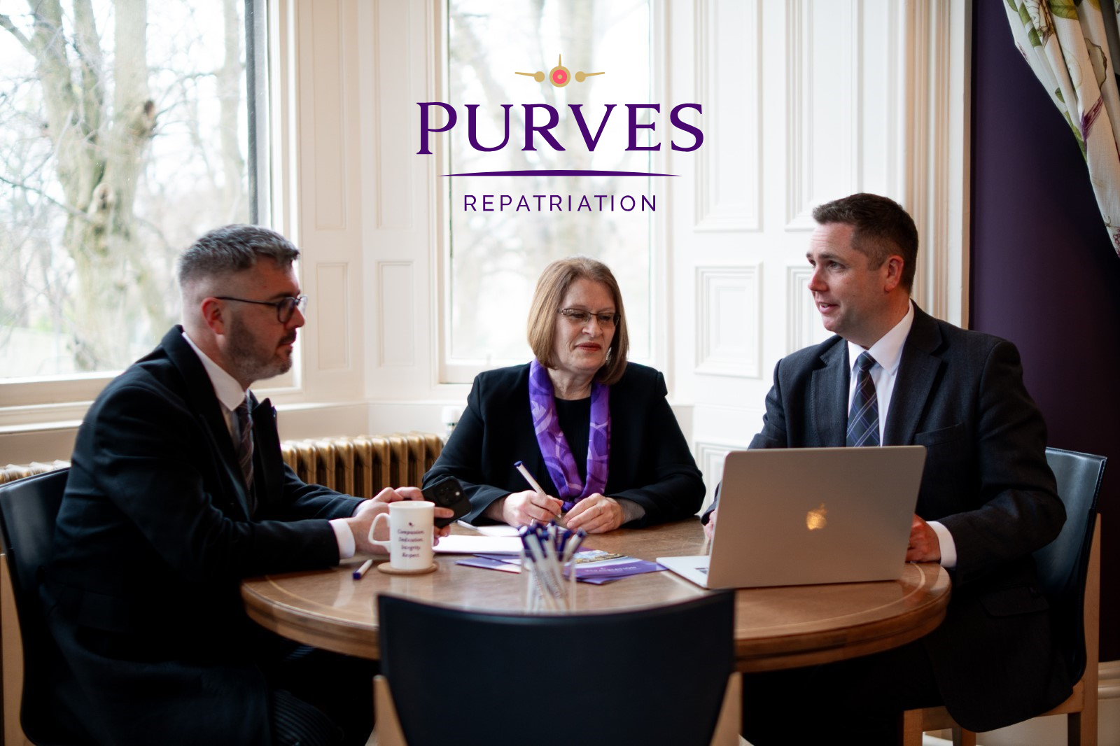 The purves repatriation team sat at a desk in front of a bay window having a meeting