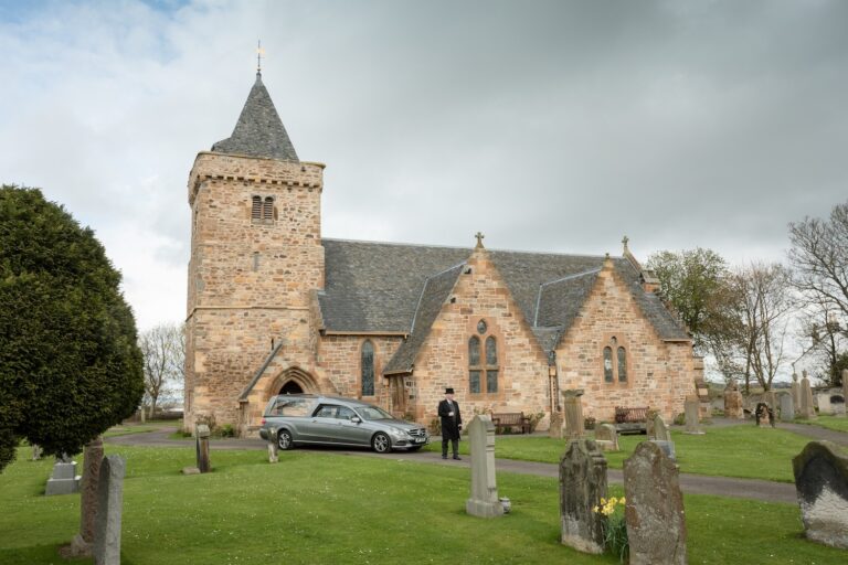 Aberlady Parish Church with a funeral car outside and officiant .