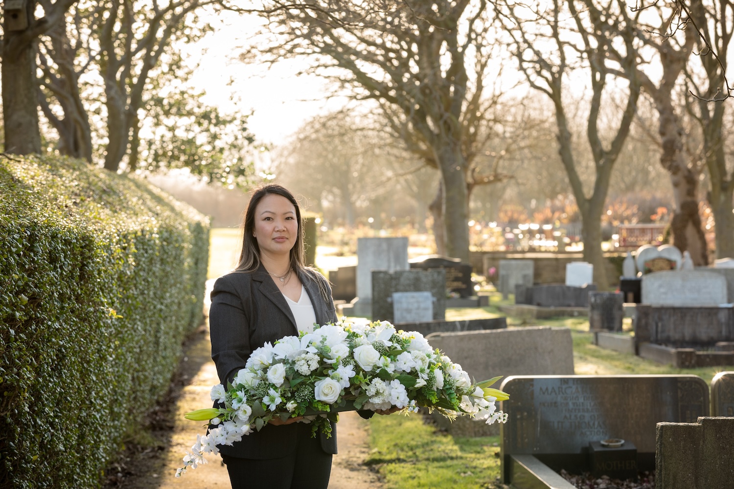 A funeral director standing with a floral arrangement in her hands with the sun behind them