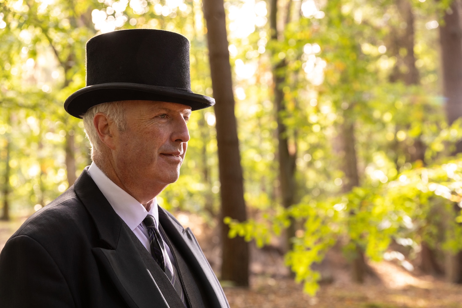 A man wearing a top hat standing in a wooded area